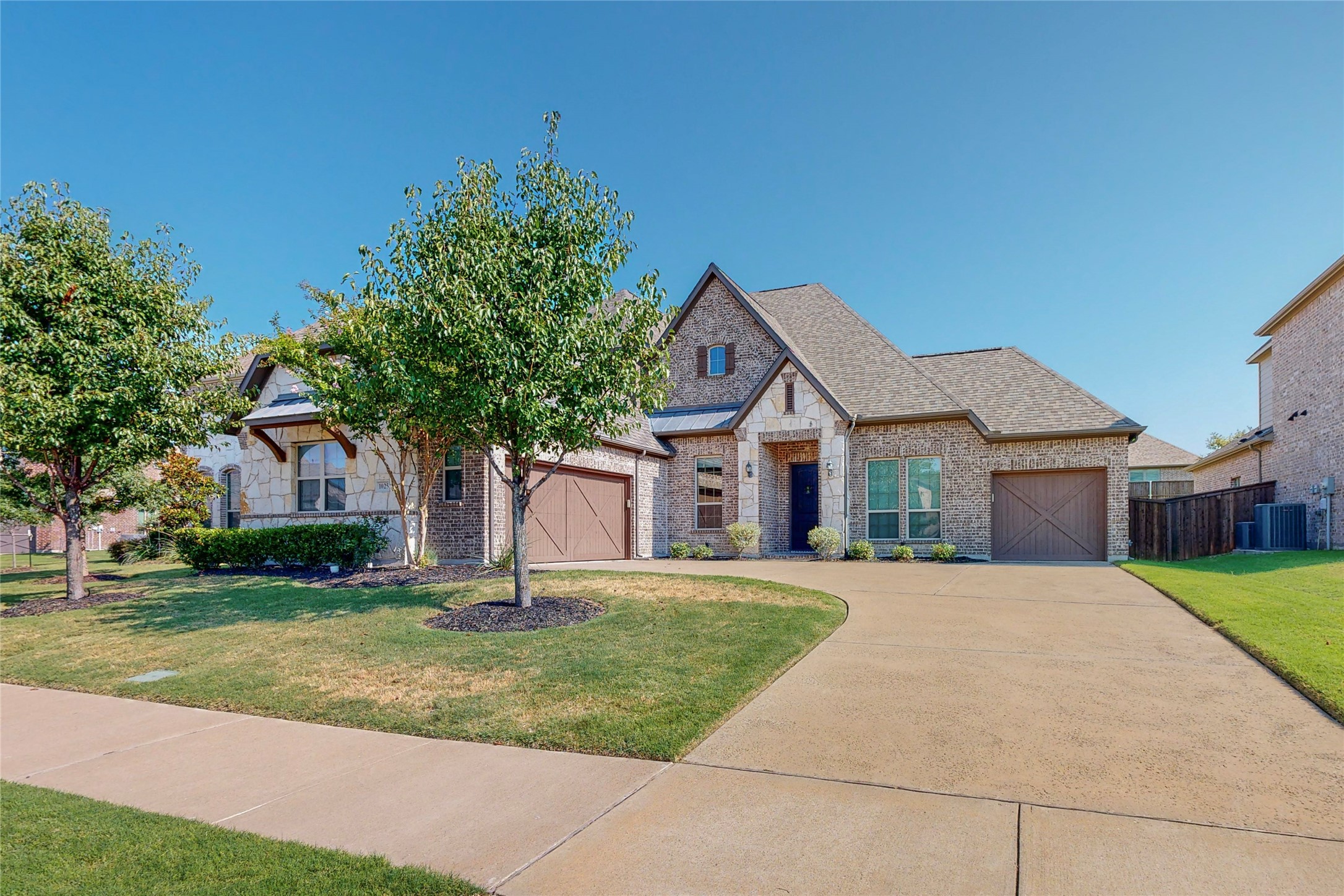 Brick-and-stone house with two garage doors, a broad driveway, and landscaped front lawn.