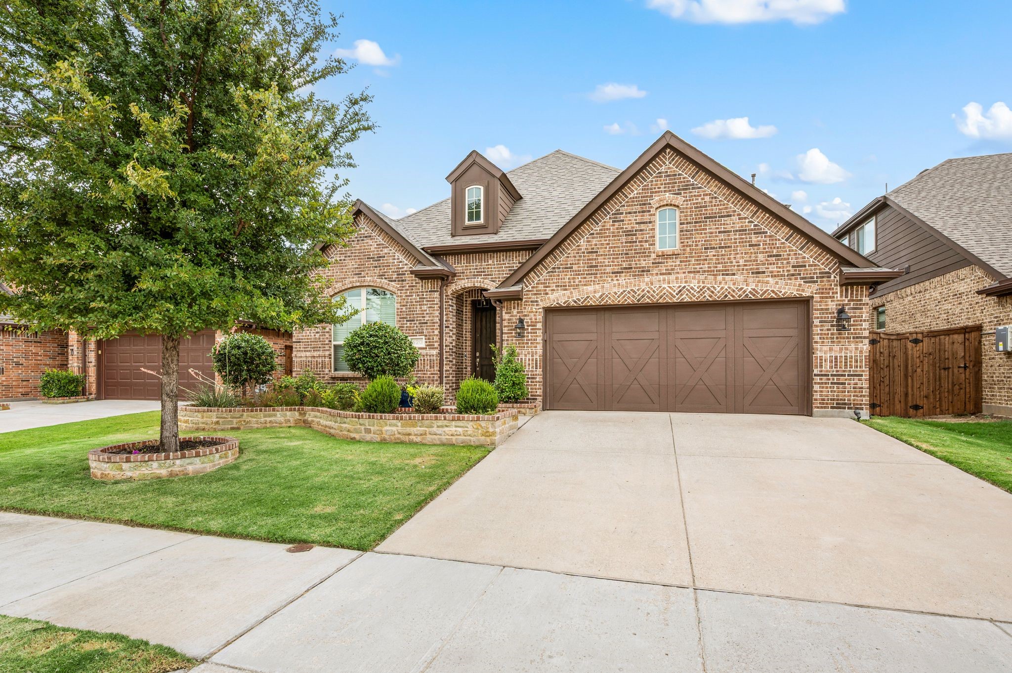 Brick house with a brown double garage, landscaped front yard, and mature tree.