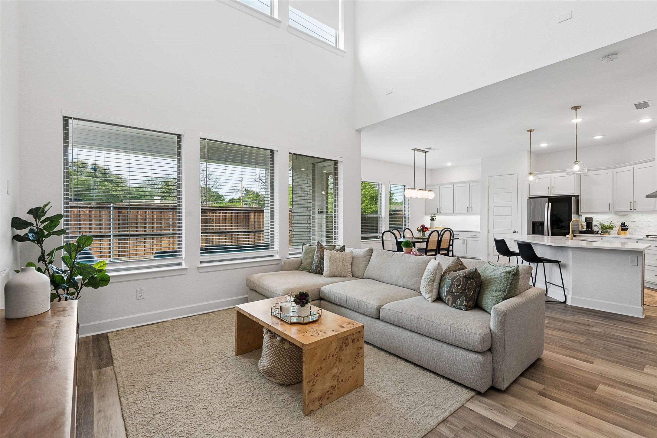 Open-plan living room with a gray sectional, vaulted ceiling, and adjoining white kitchen.