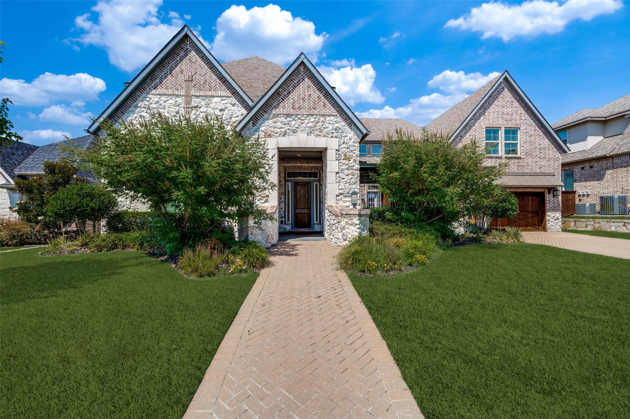 Two-story stone-and-brick house with steep gables, landscaped lawn, and brick walkway to the front entrance.