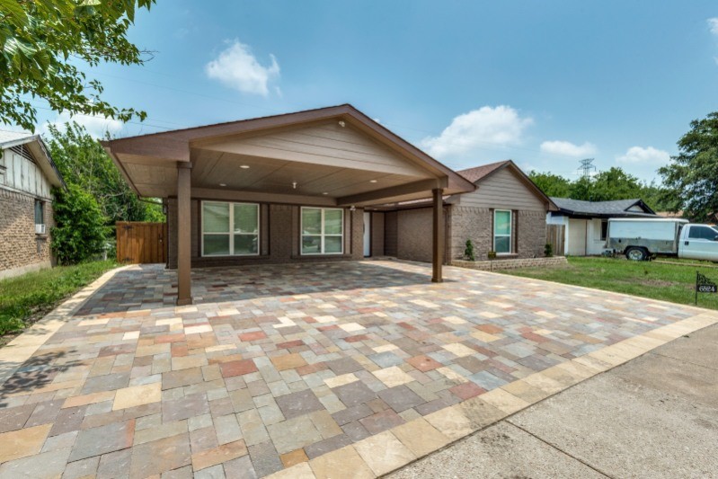 Single-story home with a wide covered carport and multicolored paver parking area.