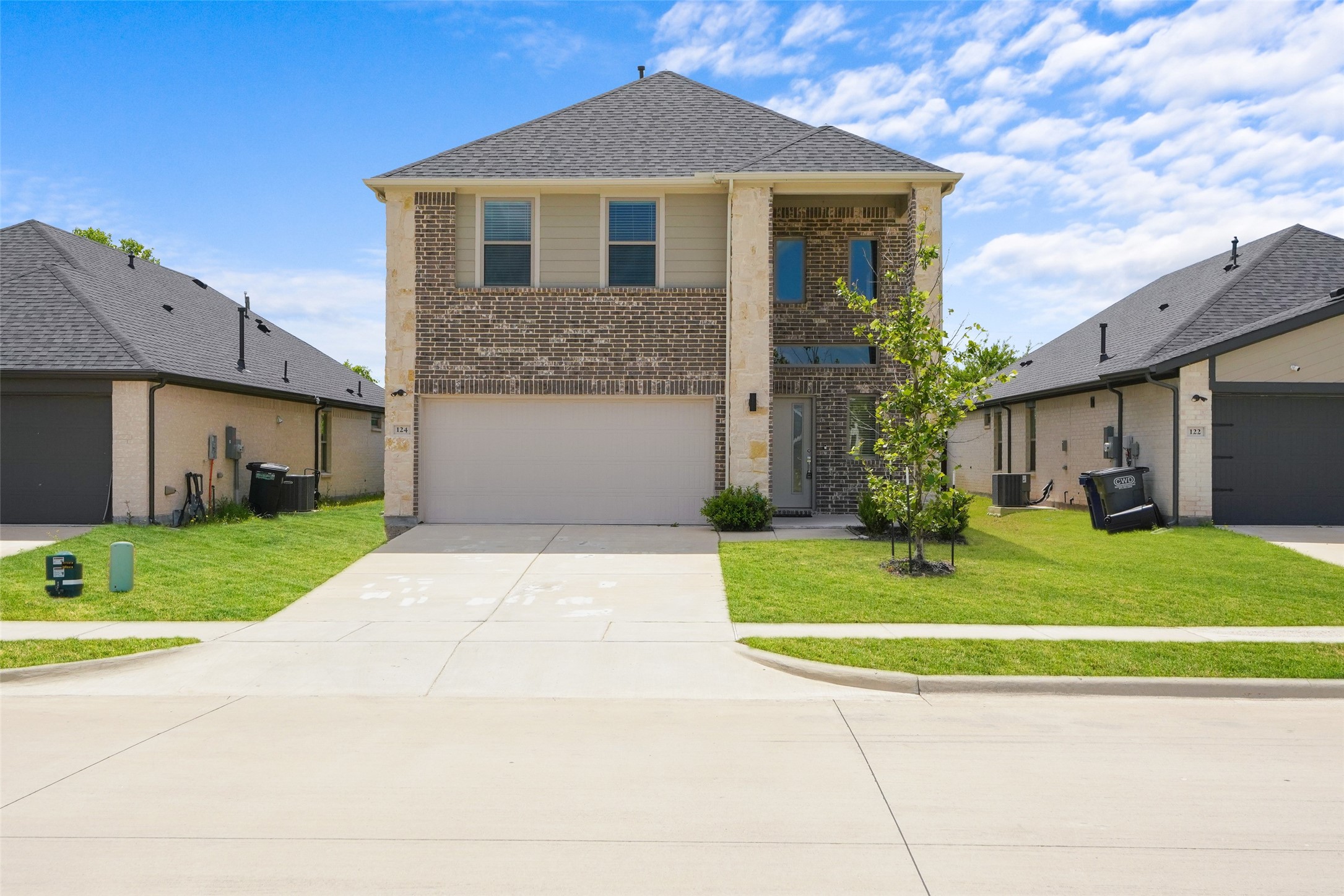 Two-story brick-and-stone house with a double garage, broad driveway, and young tree in the front lawn.