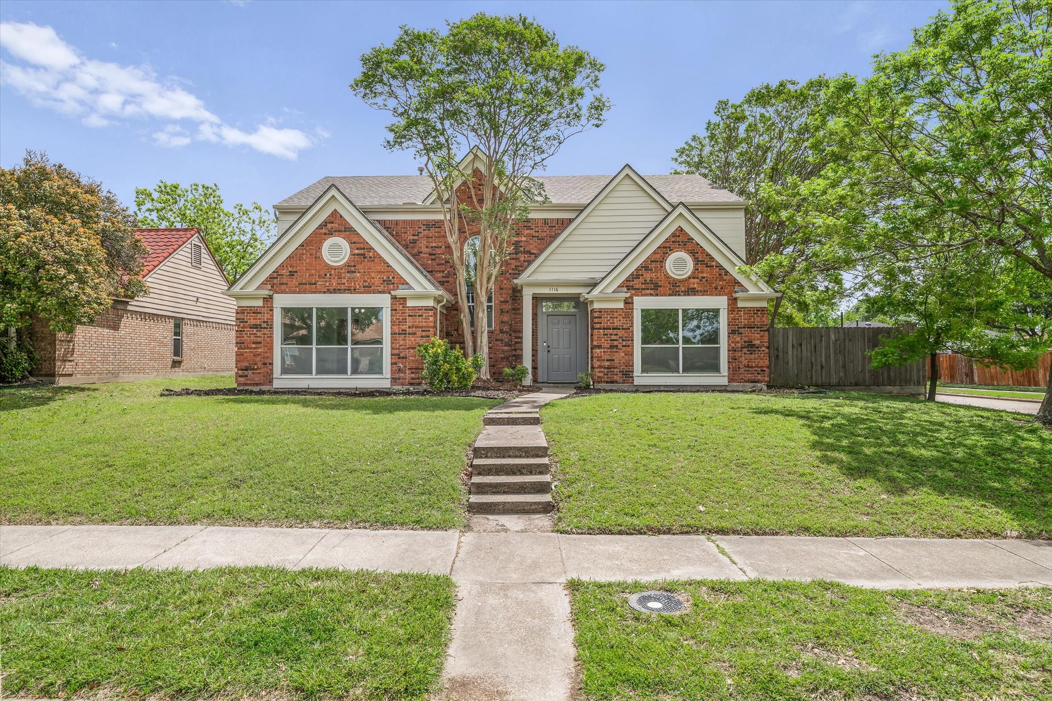 Two-story red brick house with cream gables and a front walkway through the lawn.