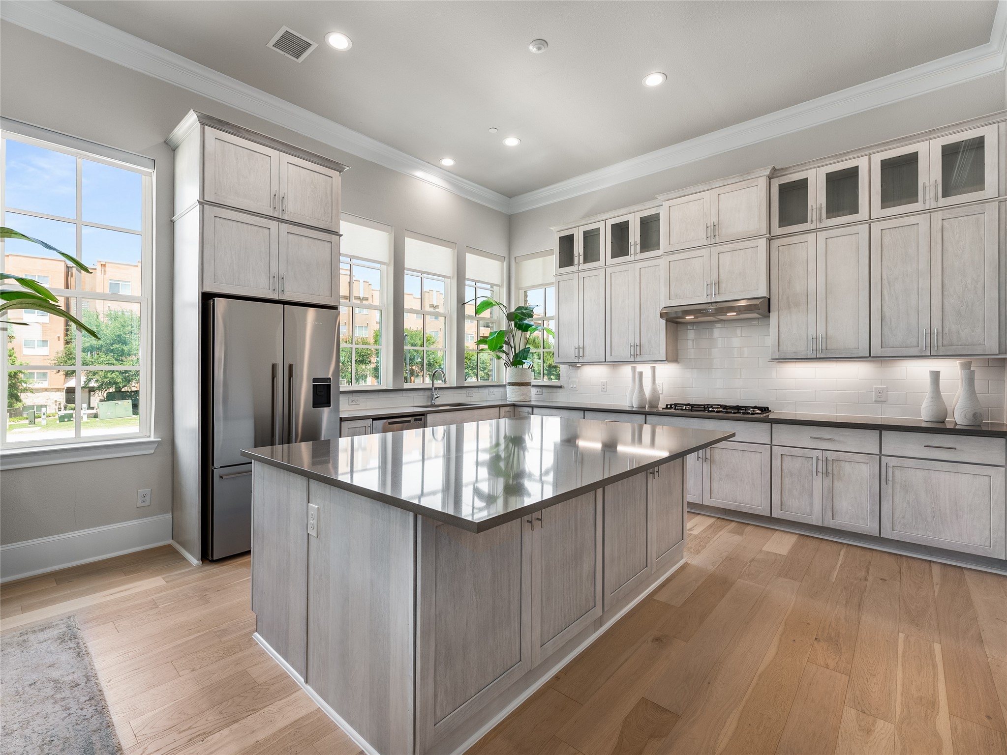 Bright kitchen with a large reflective island, light cabinetry, stainless steel appliances, and tall windows.