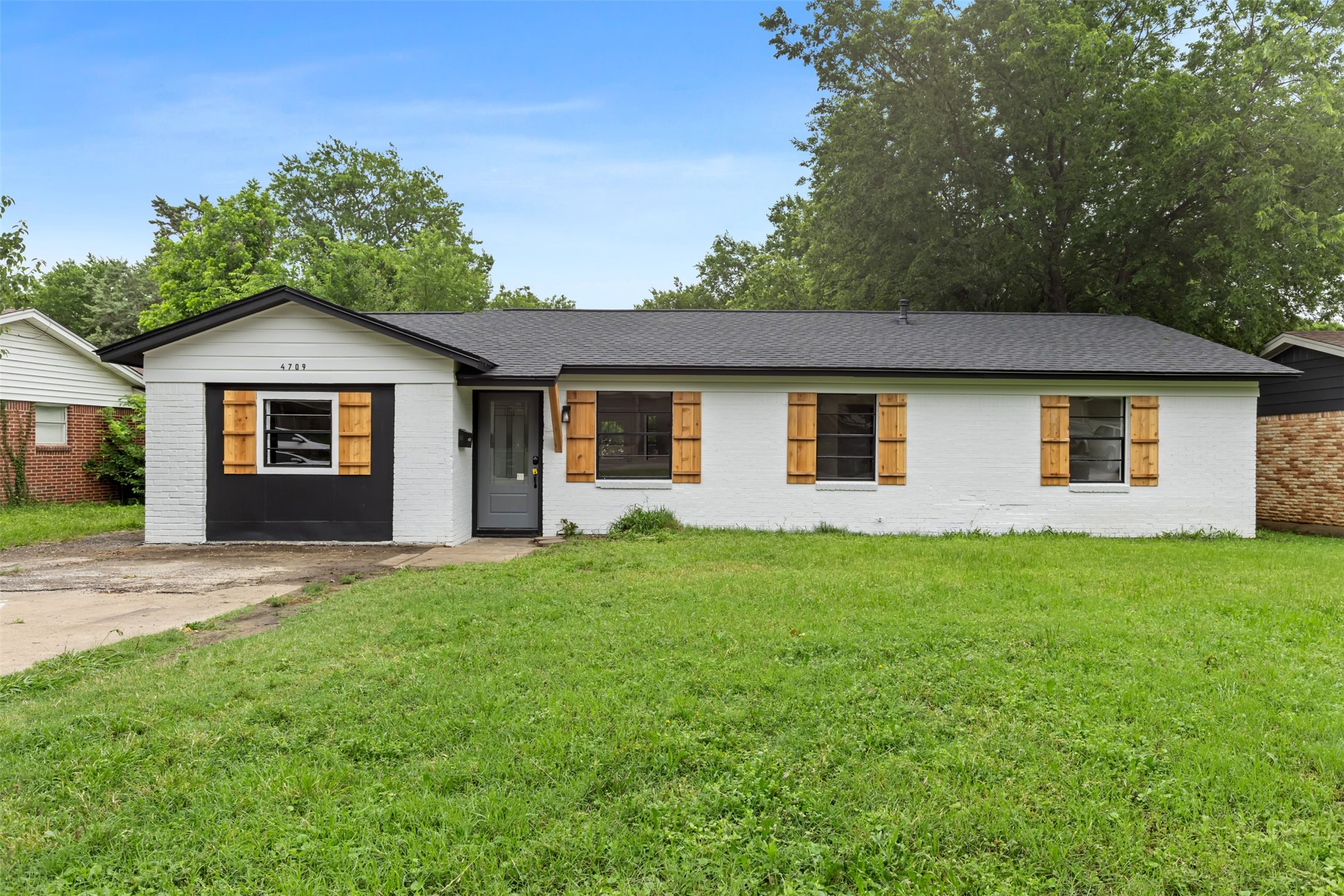 White brick ranch house with dark trim, wood shutters, and a wide green lawn.