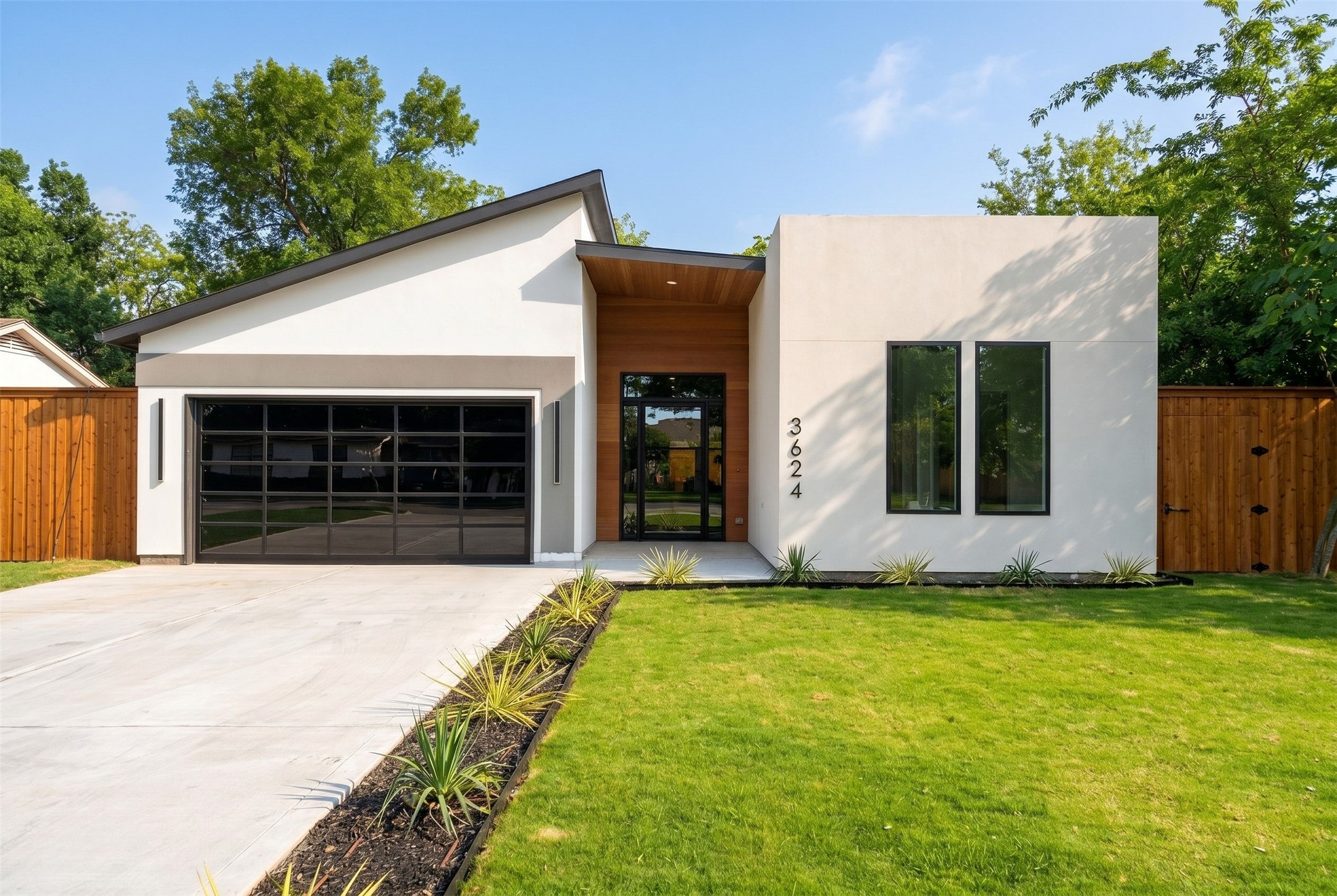 Modern white house with wood-paneled entry, glass garage door, landscaped lawn, and wooden privacy fence.