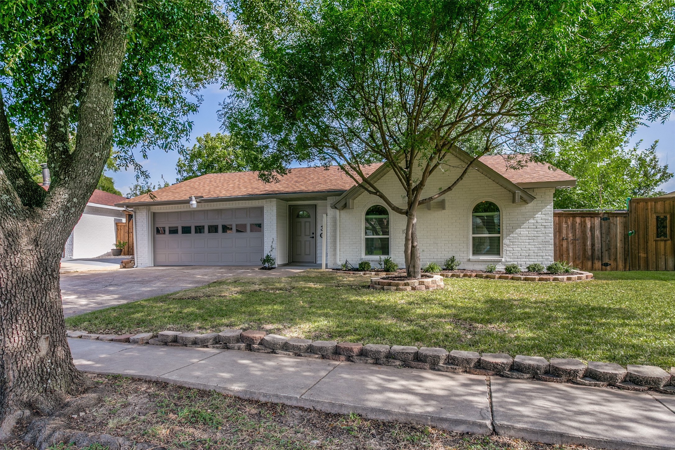 White brick house with arched windows and an attached garage, shaded by mature trees.