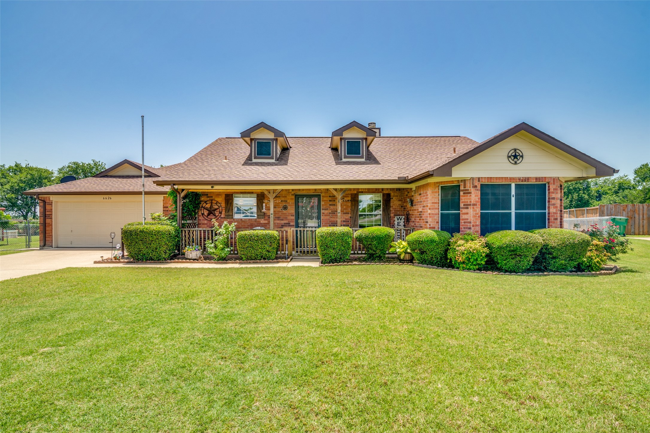Single-story brick house with two roof dormers, a covered porch, trimmed hedges, and a wide lawn.