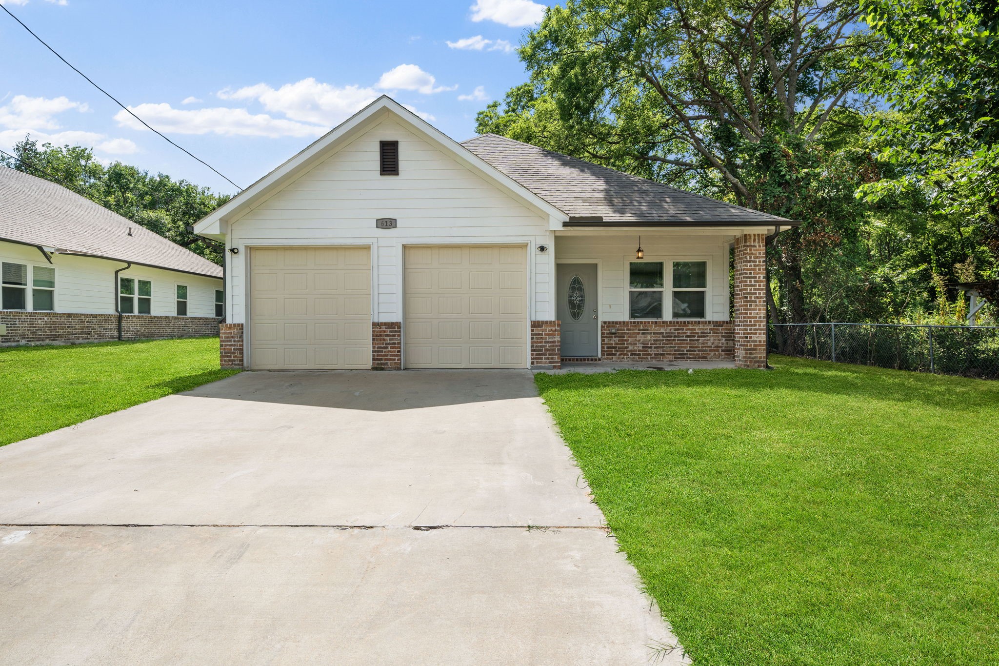 White single-story house with brick accents, two garage doors, and a wide concrete driveway.
