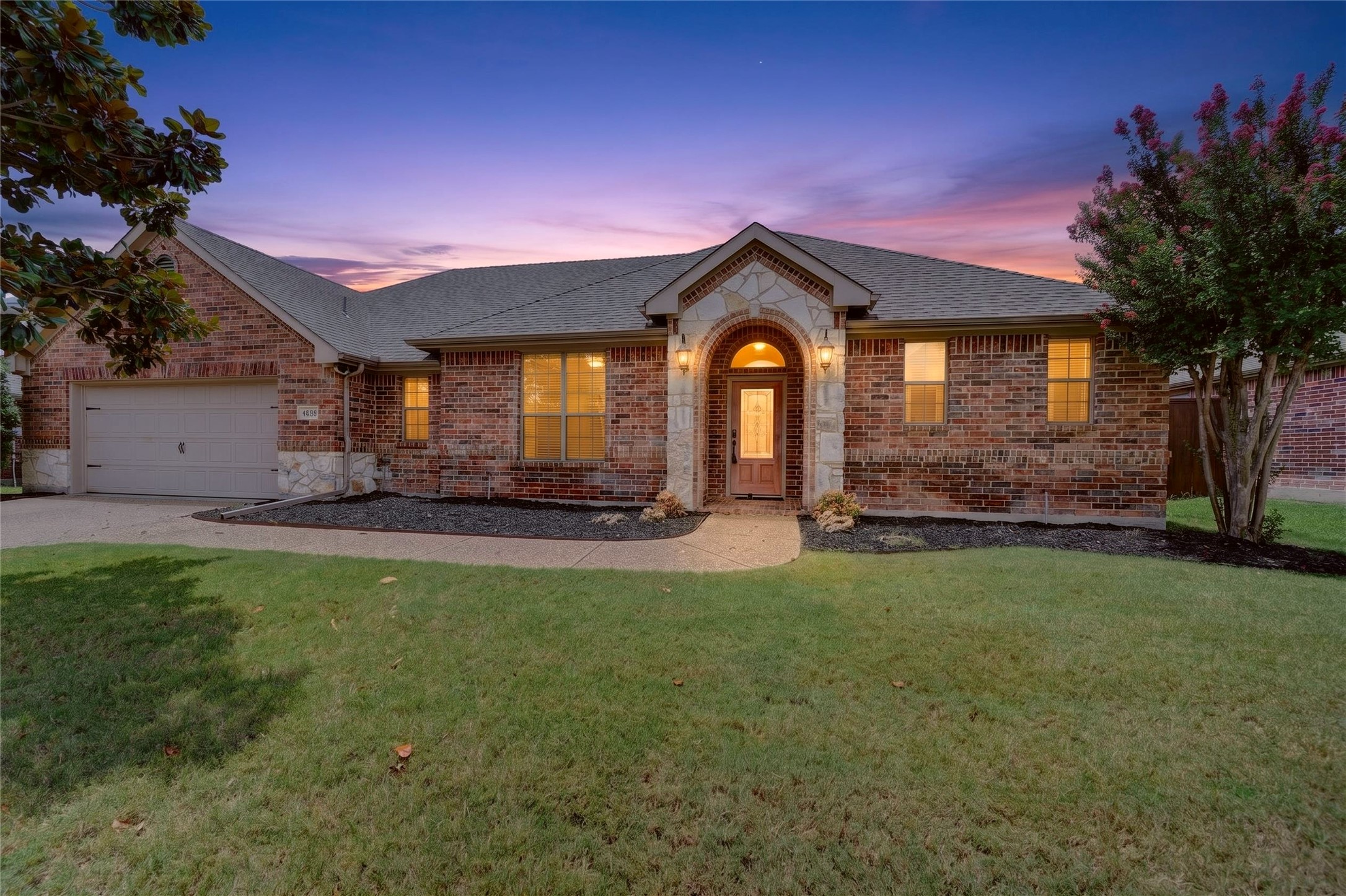Brick ranch house with an arched stone-trimmed entrance and glowing windows at dusk.