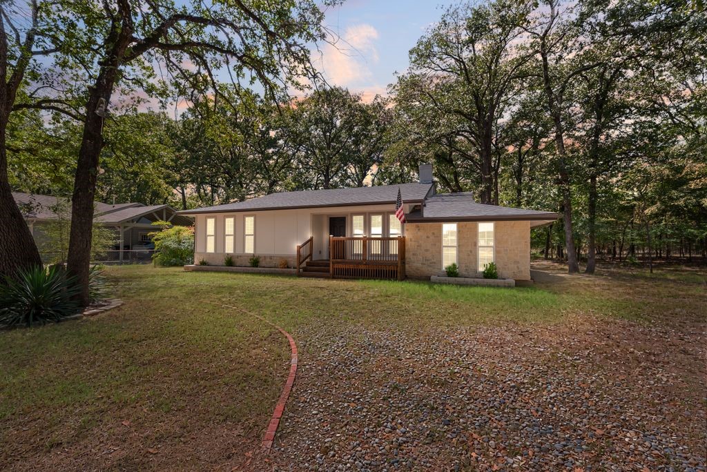 Single-story ranch house with a stone facade and wooden porch on a wooded lot at dusk.