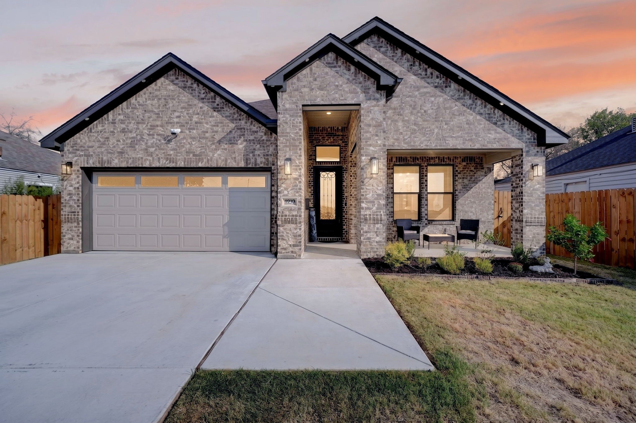 Brick house at dusk with multiple gables, a gray garage door, and a covered front porch.