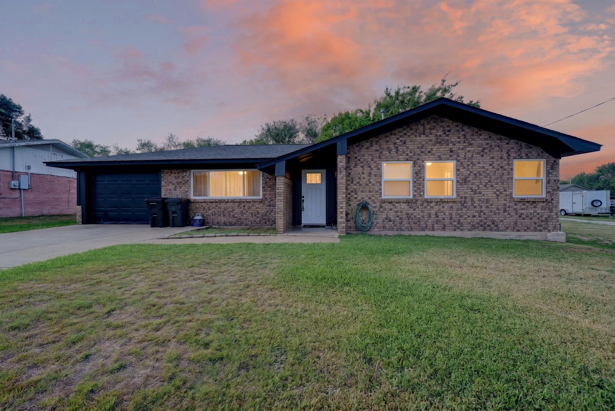 Single-story brick house with an attached garage and warmly lit windows at dusk.