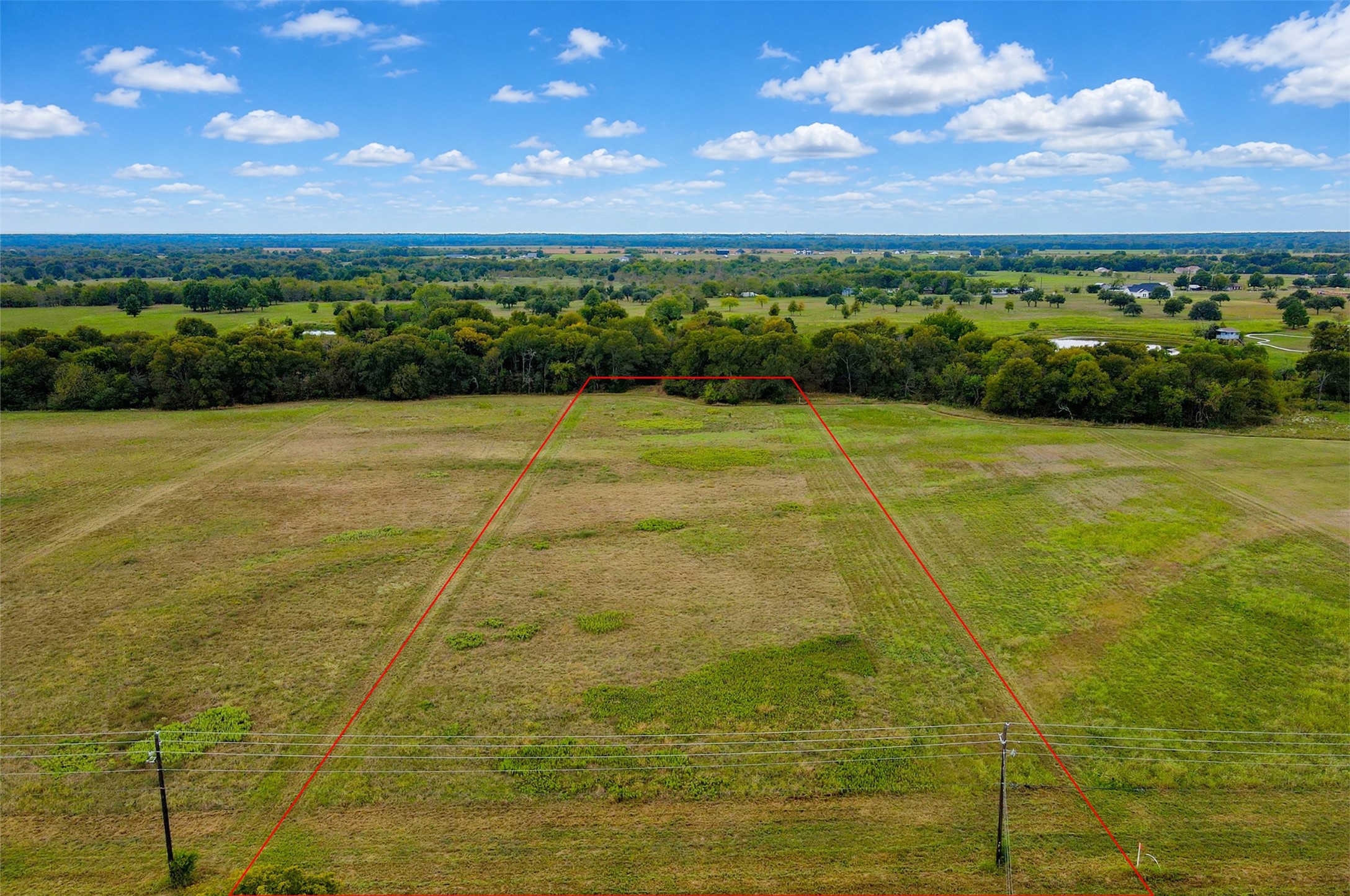 Aerial view of a grassy parcel outlined in red, with a fence and wooded horizon.