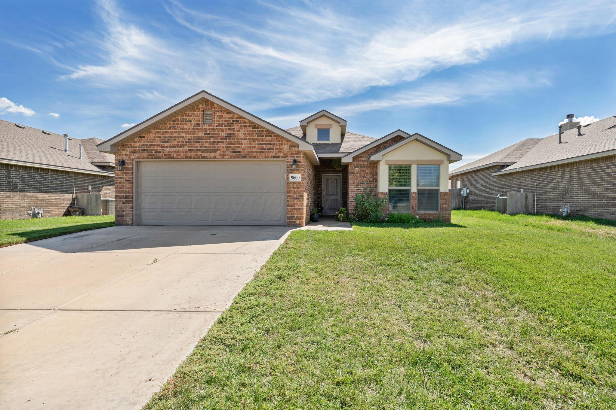 Brick house with a two-car garage, broad driveway, and green front lawn.