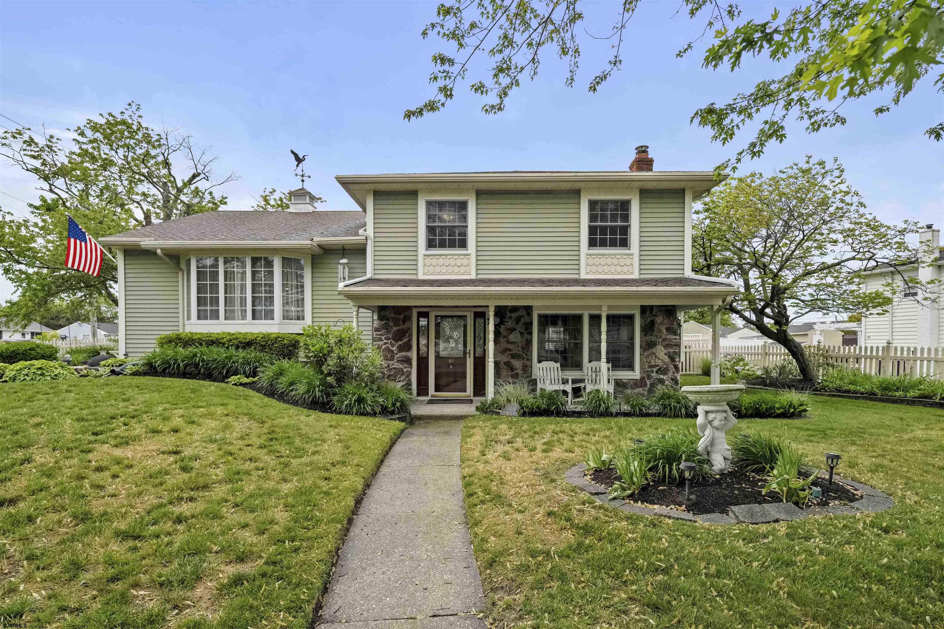 Pale green two-story home with stone facade, American flag, and landscaped front lawn.