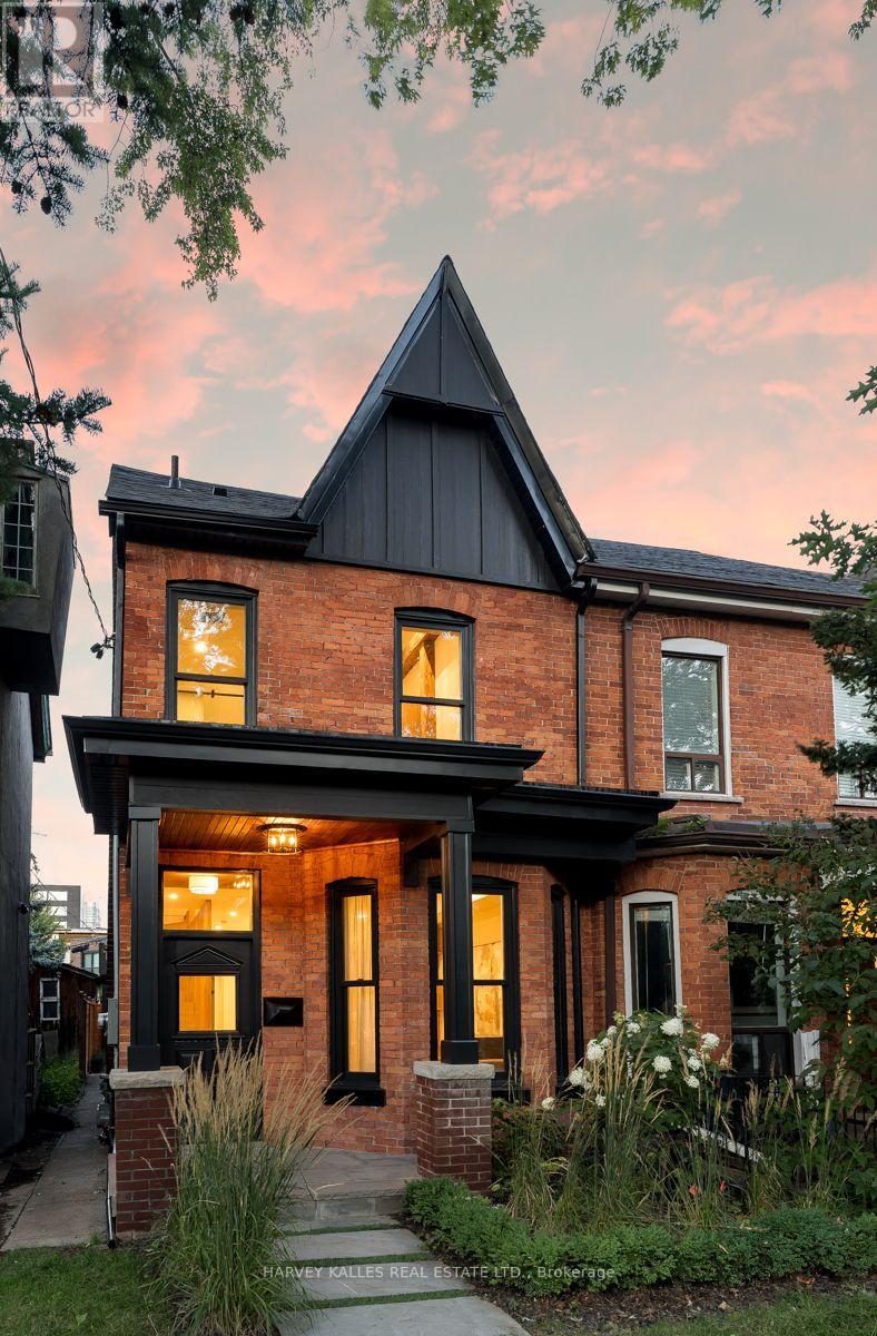 Red-brick house with a tall dark gable and warmly lit windows at dusk.