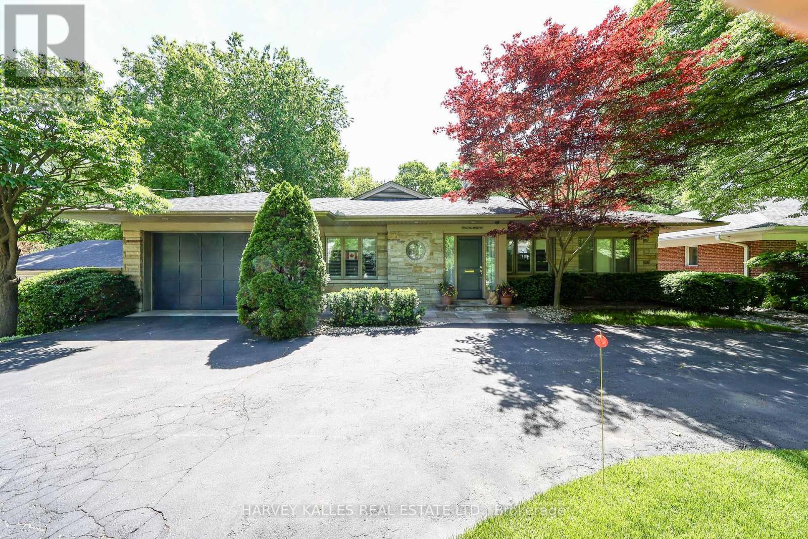 Single-story stone-front home with an attached garage, broad driveway, and mature trees.