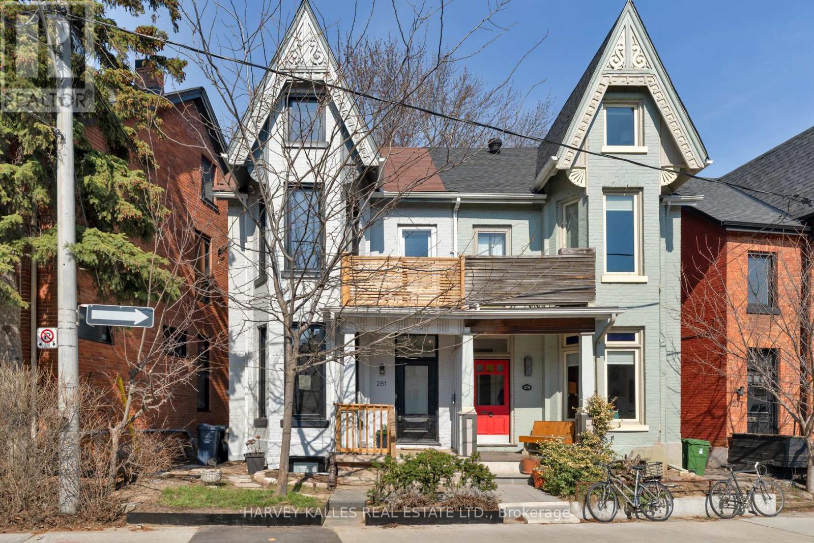 Pale blue Victorian-style house with ornate gables, a wooden balcony, and a bright red front door.