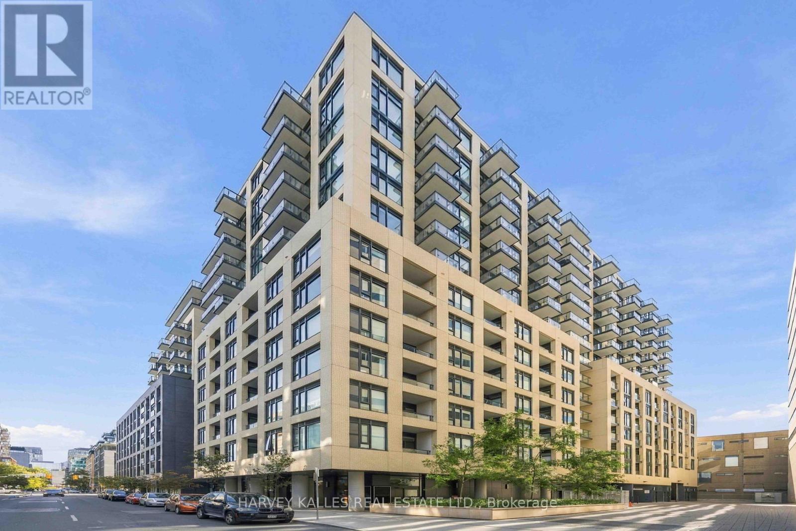 Modern beige-brick condominium tower with projecting glass balconies along a city street.