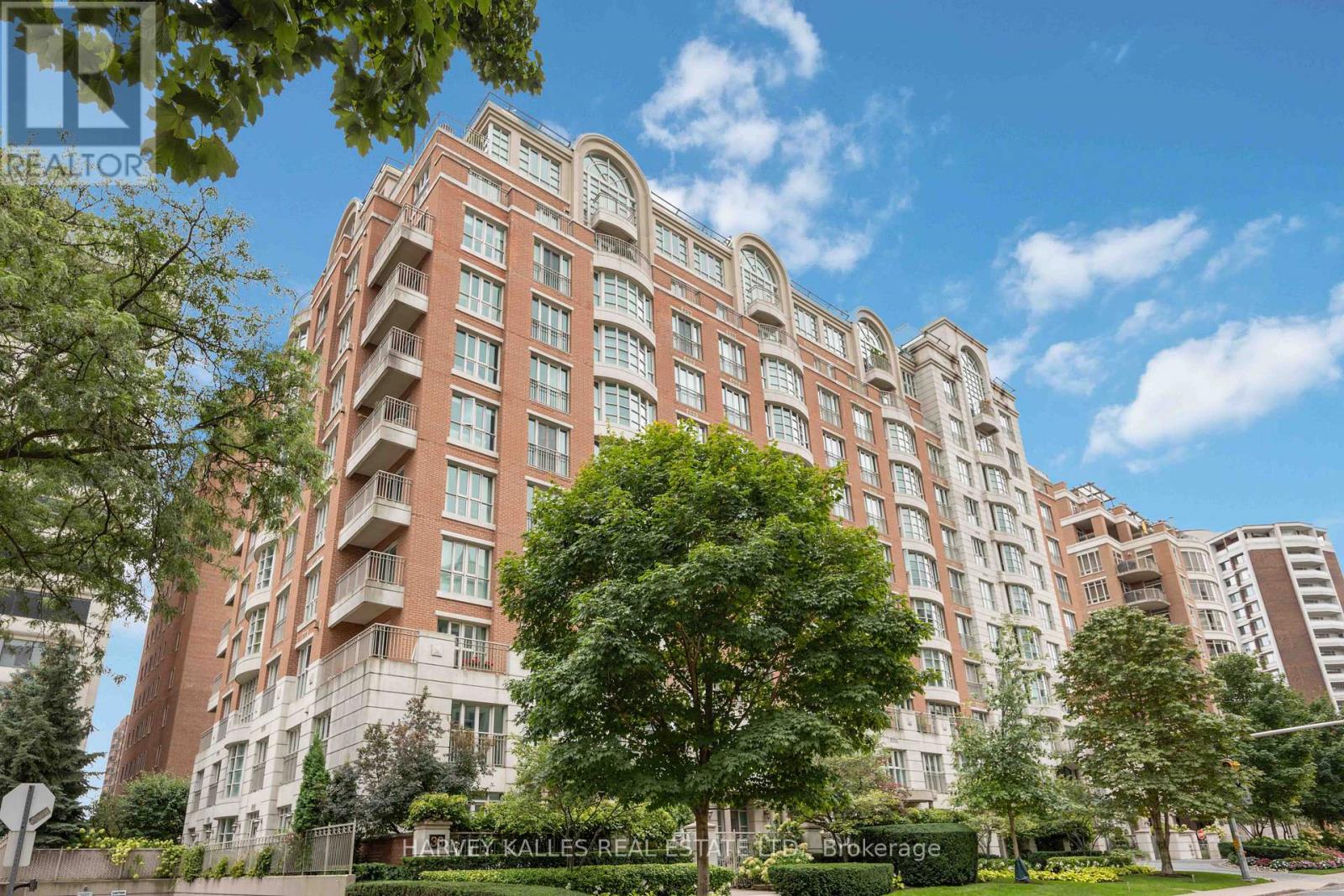 Red brick condominium with curved window bays and balconies, framed by mature trees and landscaped grounds.