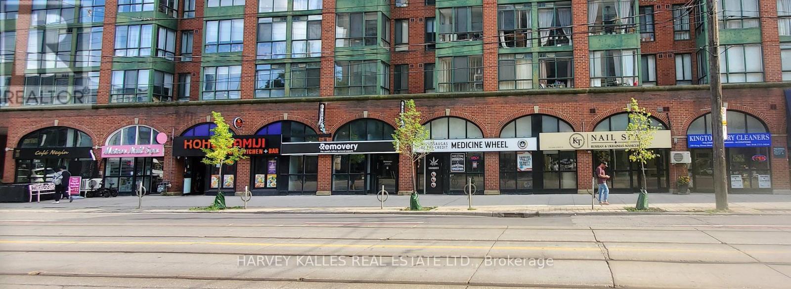 Mixed-use brick building with arched storefronts, overhead wires, and streetcar tracks in front.