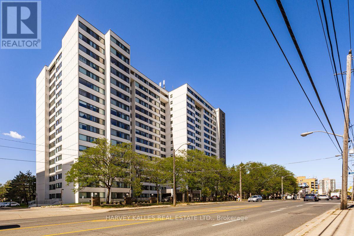 White high-rise condominium beside a tree-lined street, photographed from across the road.
