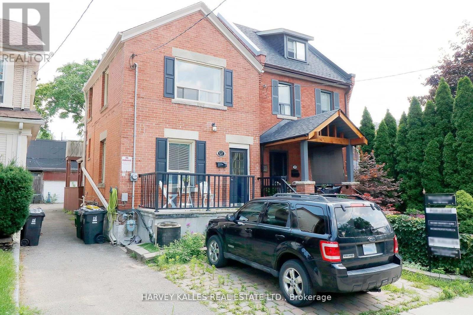Two-story red-brick house with blue shutters and a covered wooden porch, viewed from the driveway.