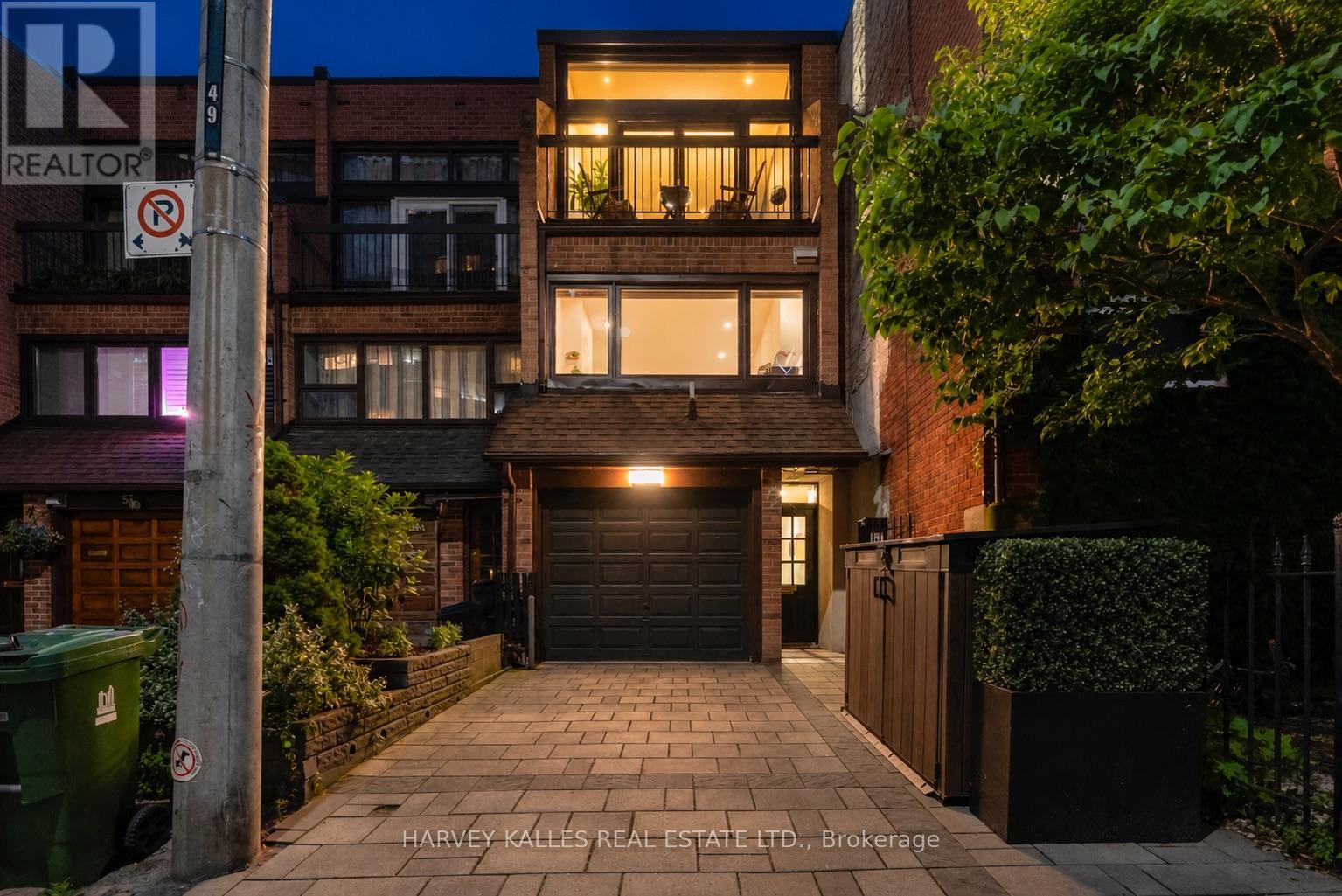 Brick townhouse at night with warmly lit windows, a garage, and a paved driveway.