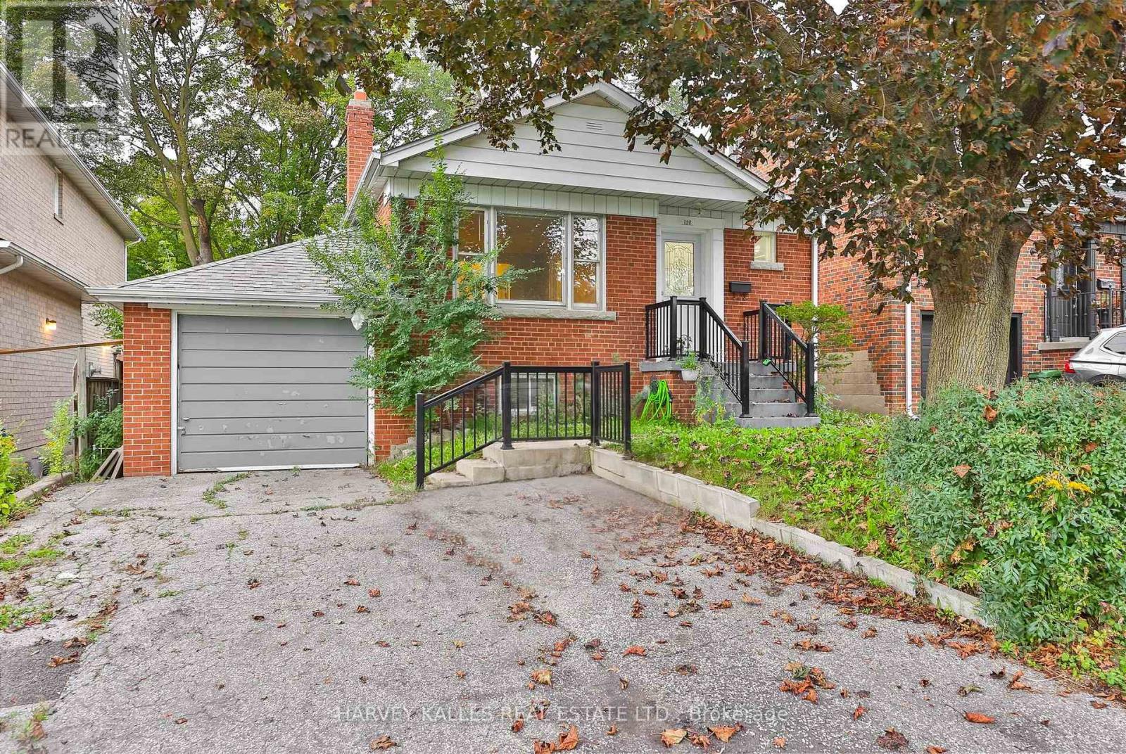 Red-brick house with a single-car garage, black entry railings, and mature autumn trees.