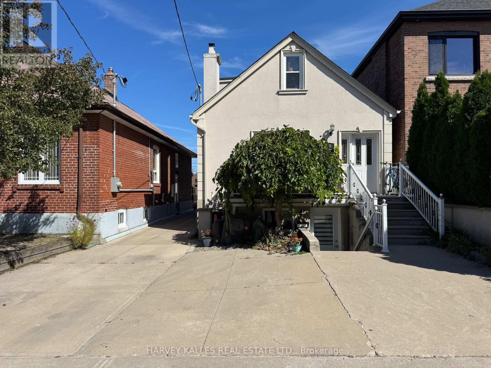 Gable-fronted house with a leafy tree partly covering its entrance and a wide concrete driveway.