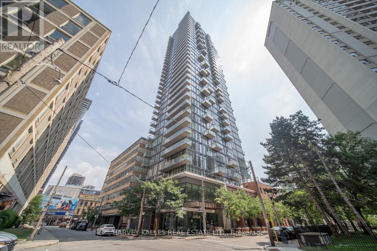 Modern glass condominium tower with projecting balconies, viewed from the street among neighboring high-rises.