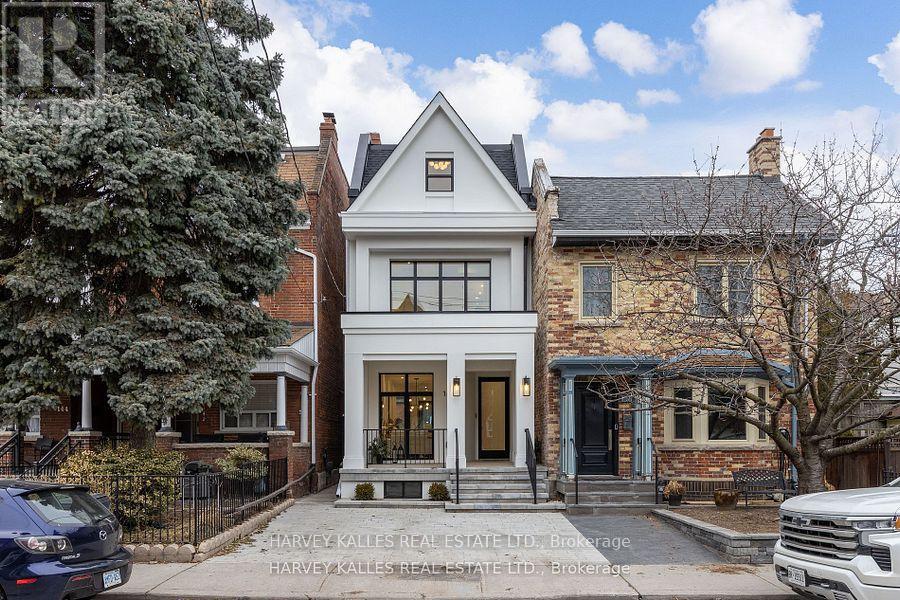 White two-storey house with a steep front gable, black-framed windows, and a covered entry between brick homes.