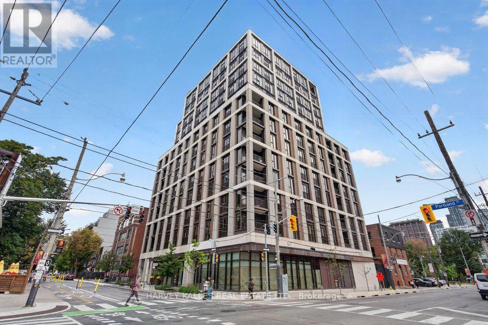 Modern mid-rise residential building at a city intersection, viewed from the corner beneath a blue sky.
