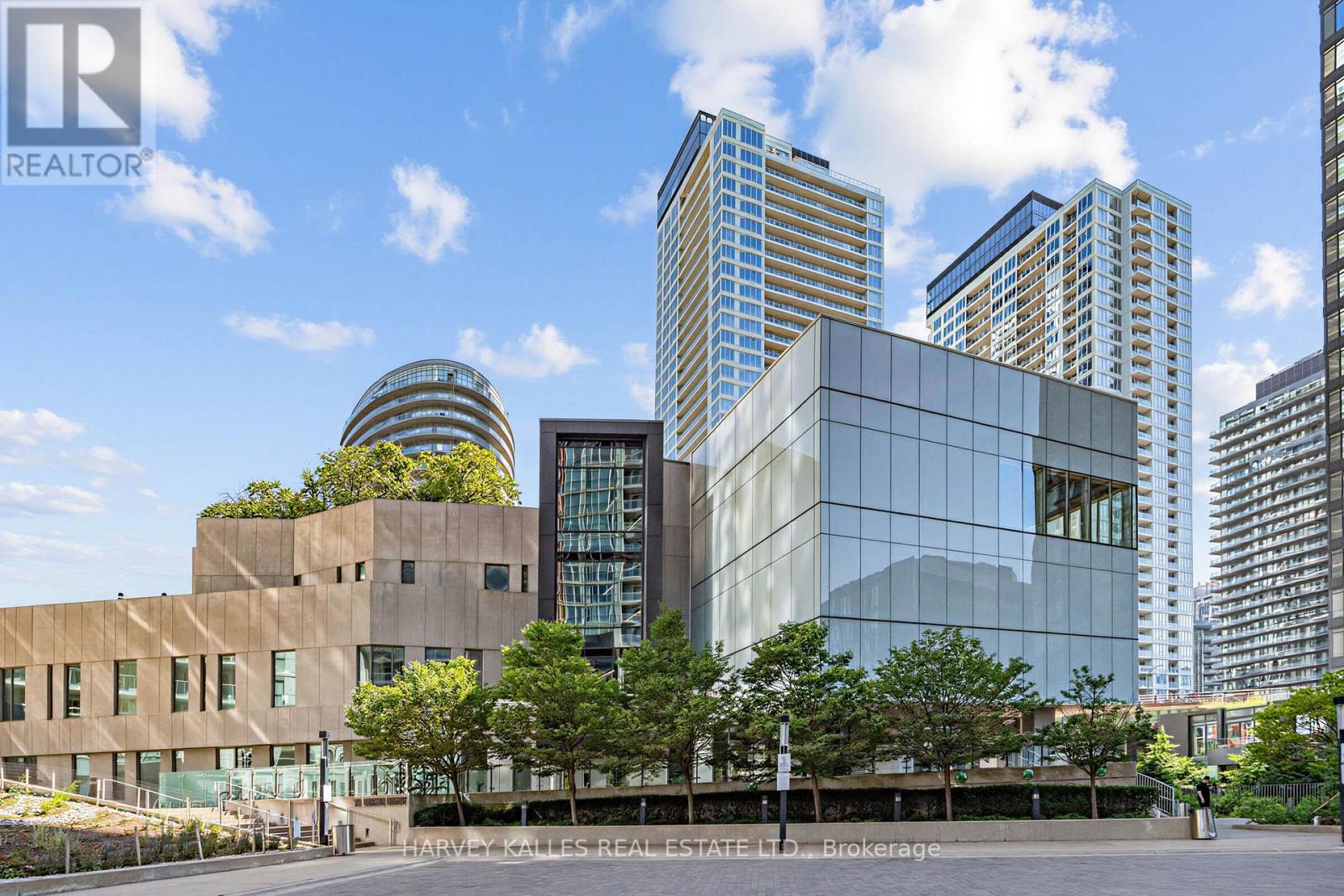 Modern urban complex with glass-fronted buildings and residential towers behind landscaped grounds.