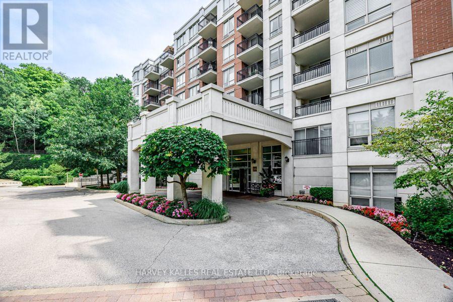 Condominium building entrance with balconies, a curved driveway, and landscaped flower beds.