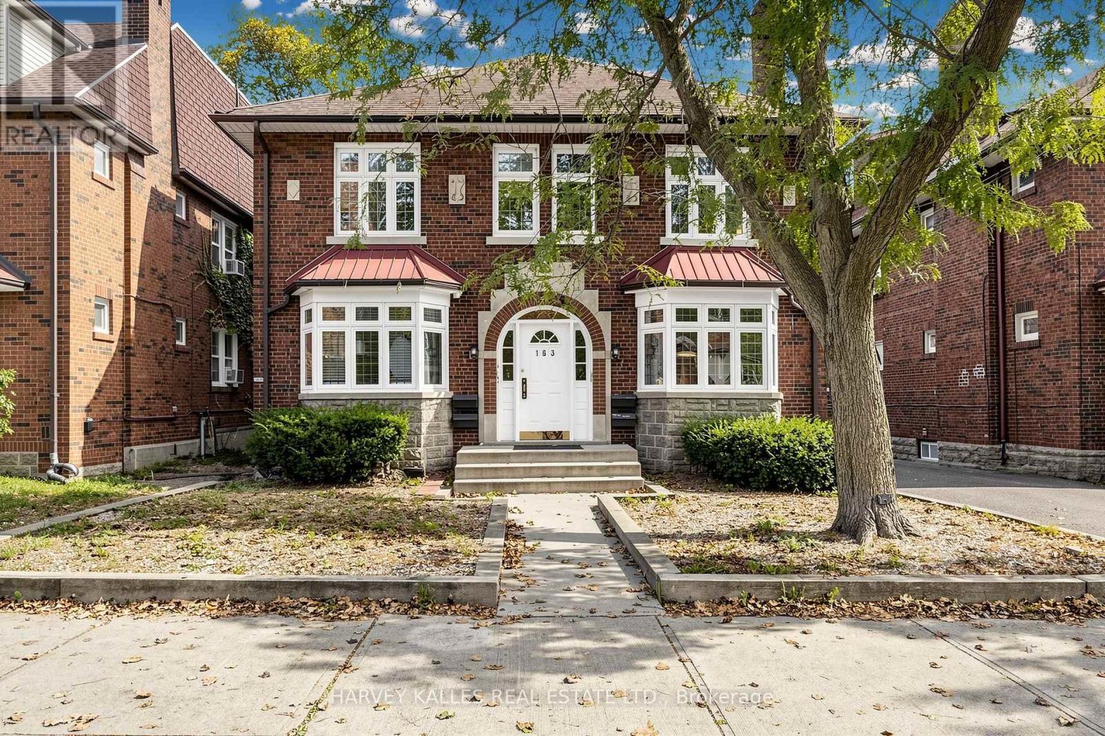 Red-brick building with white bay windows, an arched entrance marked 183, and a large tree.