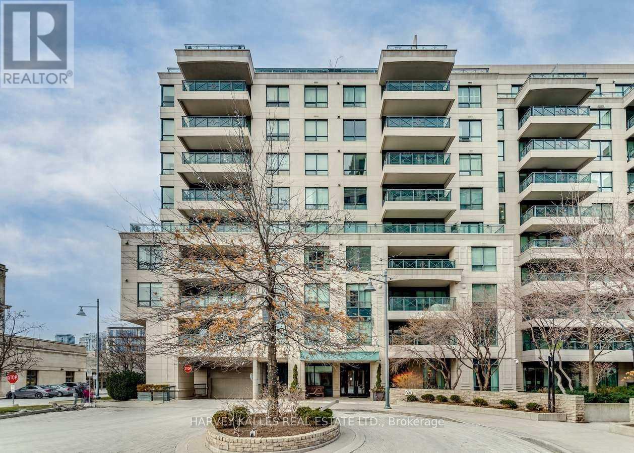 Condominium exterior with glass-railed balconies, pale stone facade, and a circular landscaped entrance island.