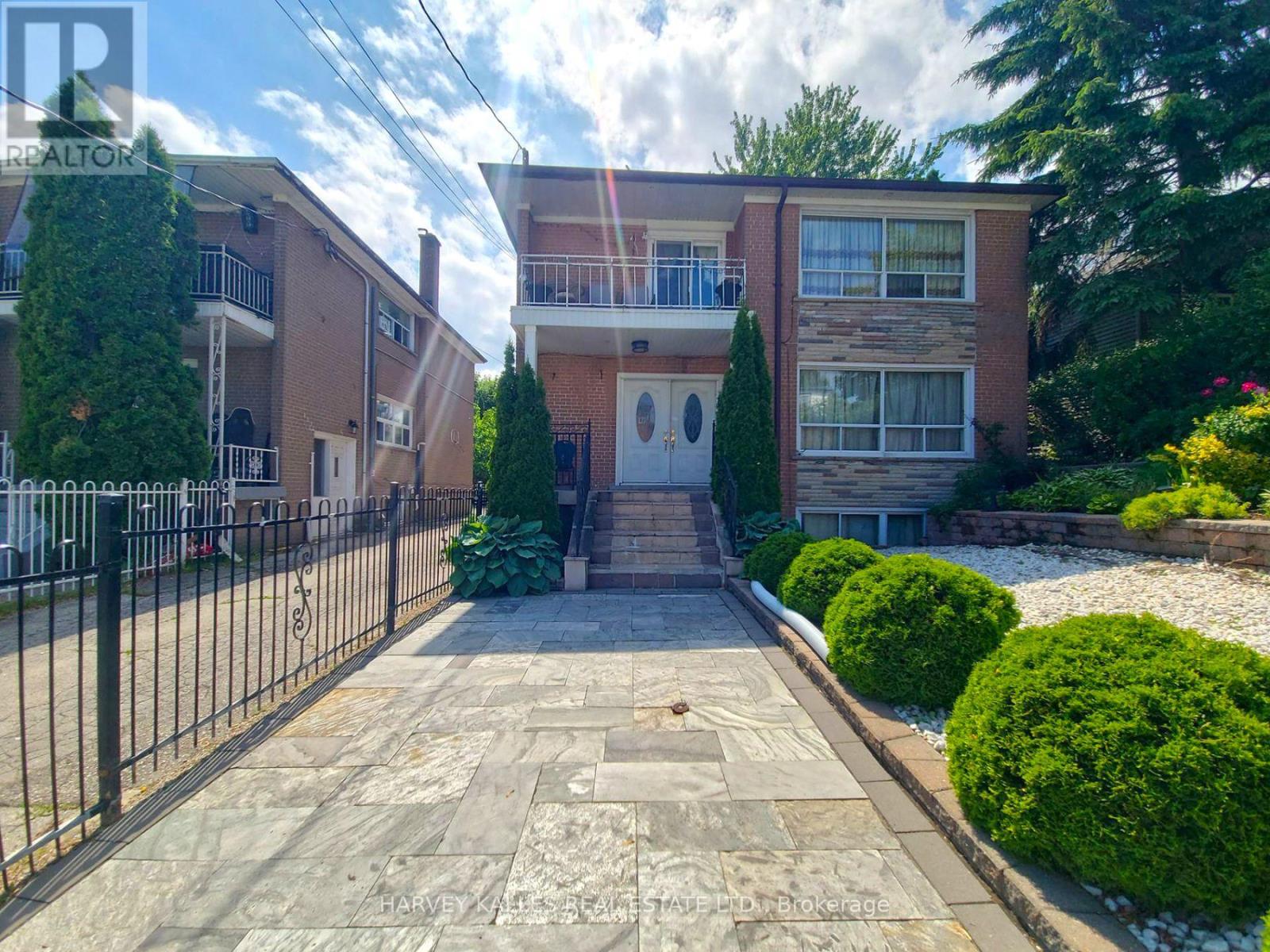 Two-storey brick house with a second-floor balcony and landscaped paved front walkway.