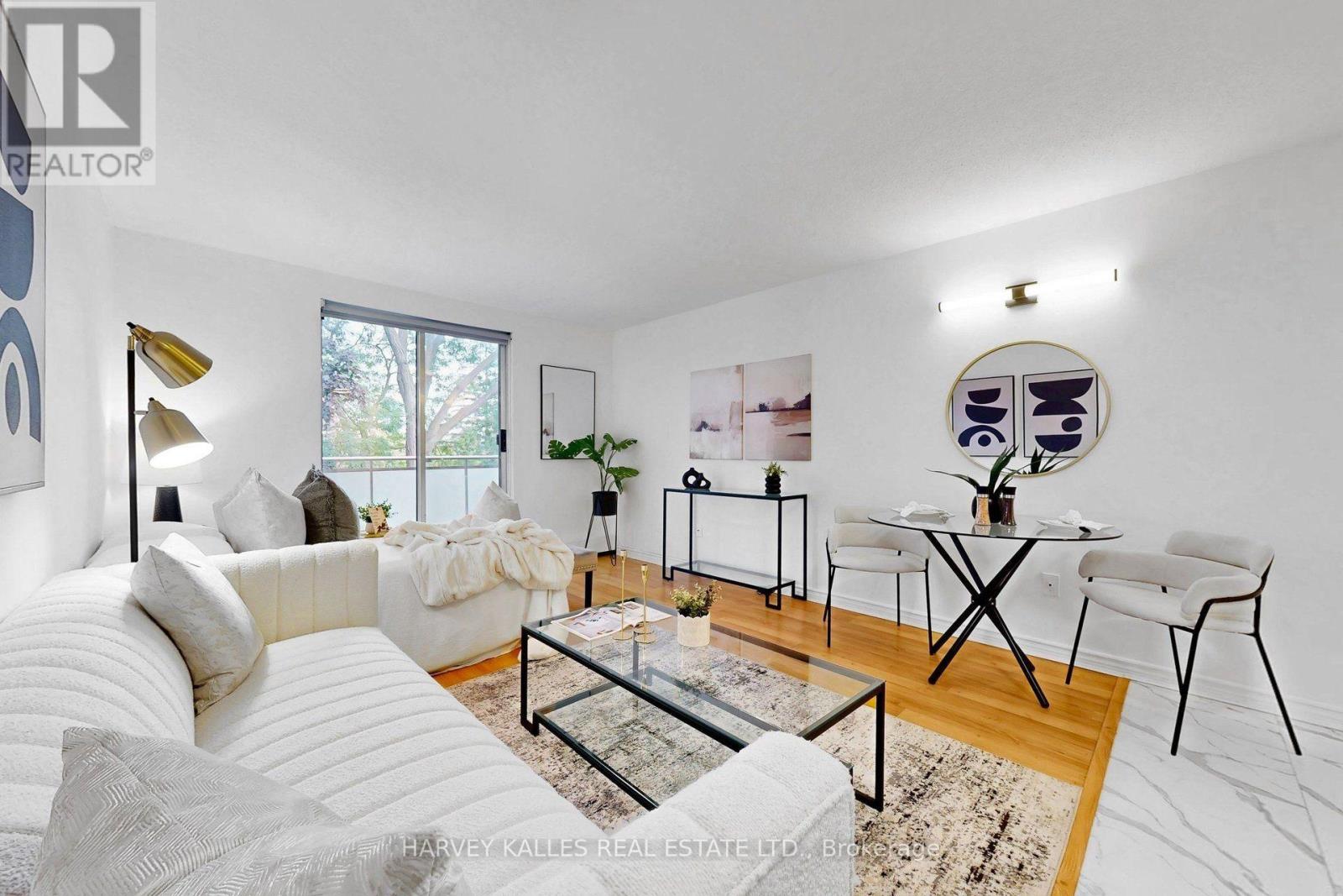 Staged living and dining room with a white sectional, glass coffee table, and balcony doors.