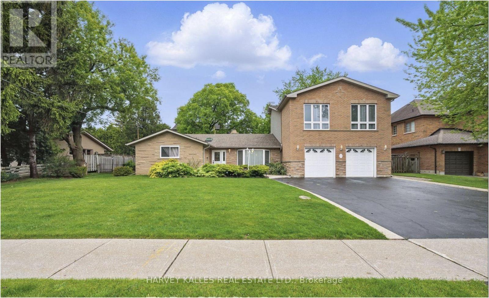 Two-storey brick house with double garage, broad lawn, mature trees, and curved driveway.