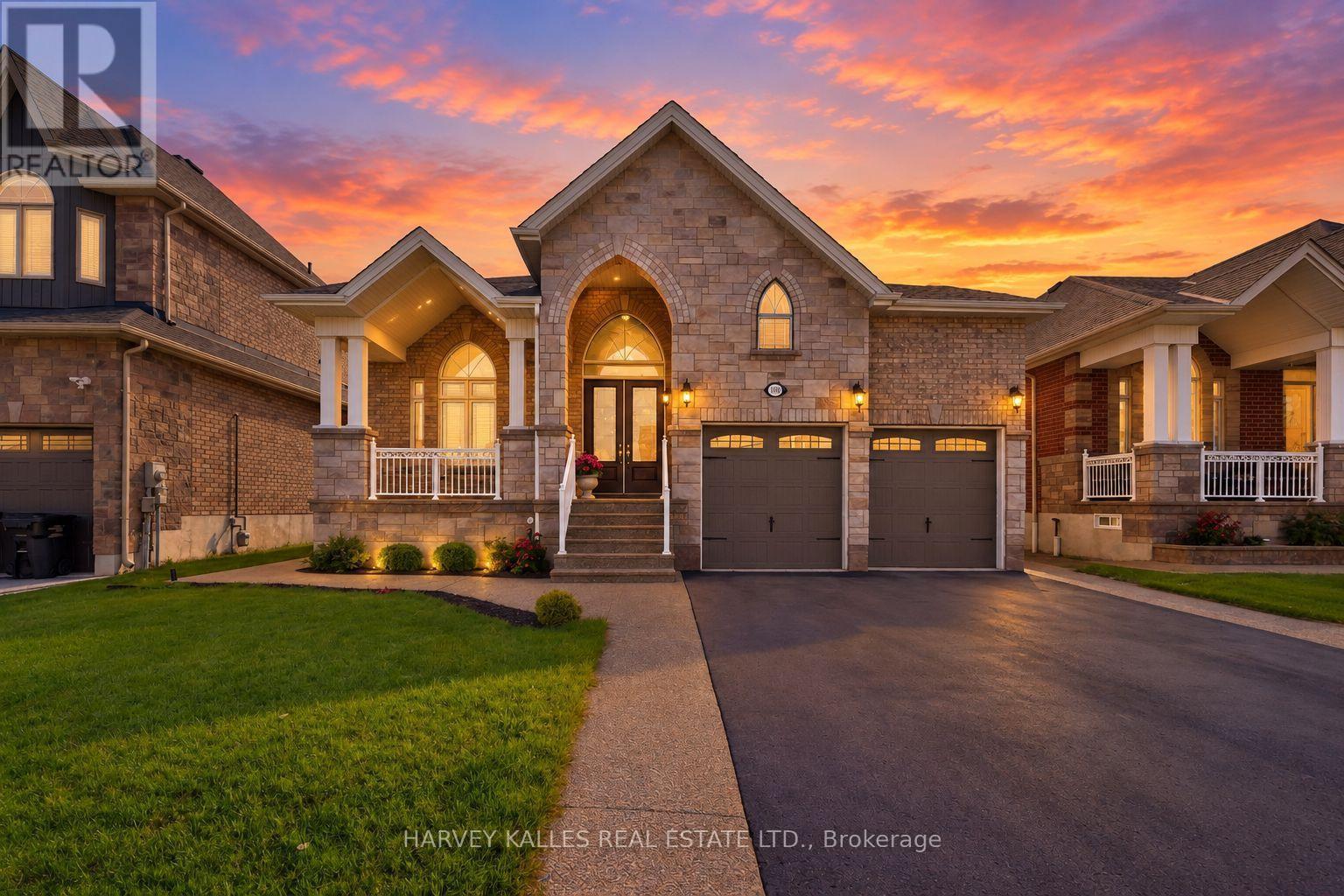 Stone-and-brick house with a double garage and arched entry beneath a vivid sunset.
