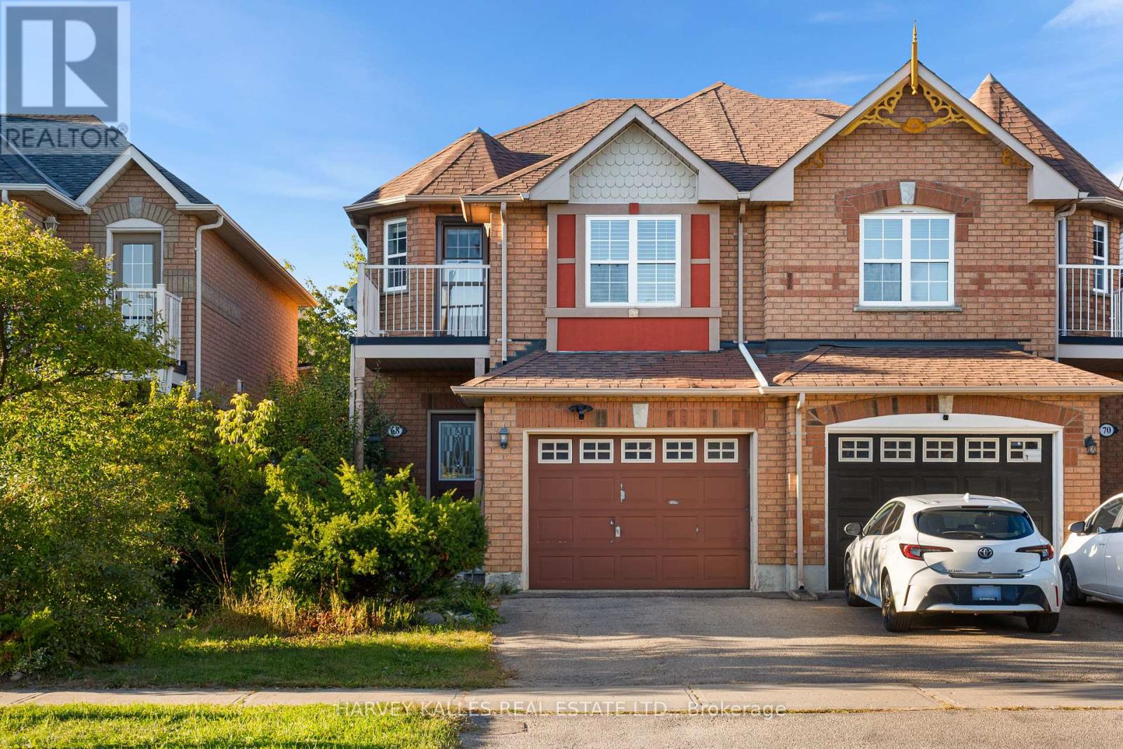 Brick townhouse with an ornate peaked gable, balconies, and cars in the driveway.