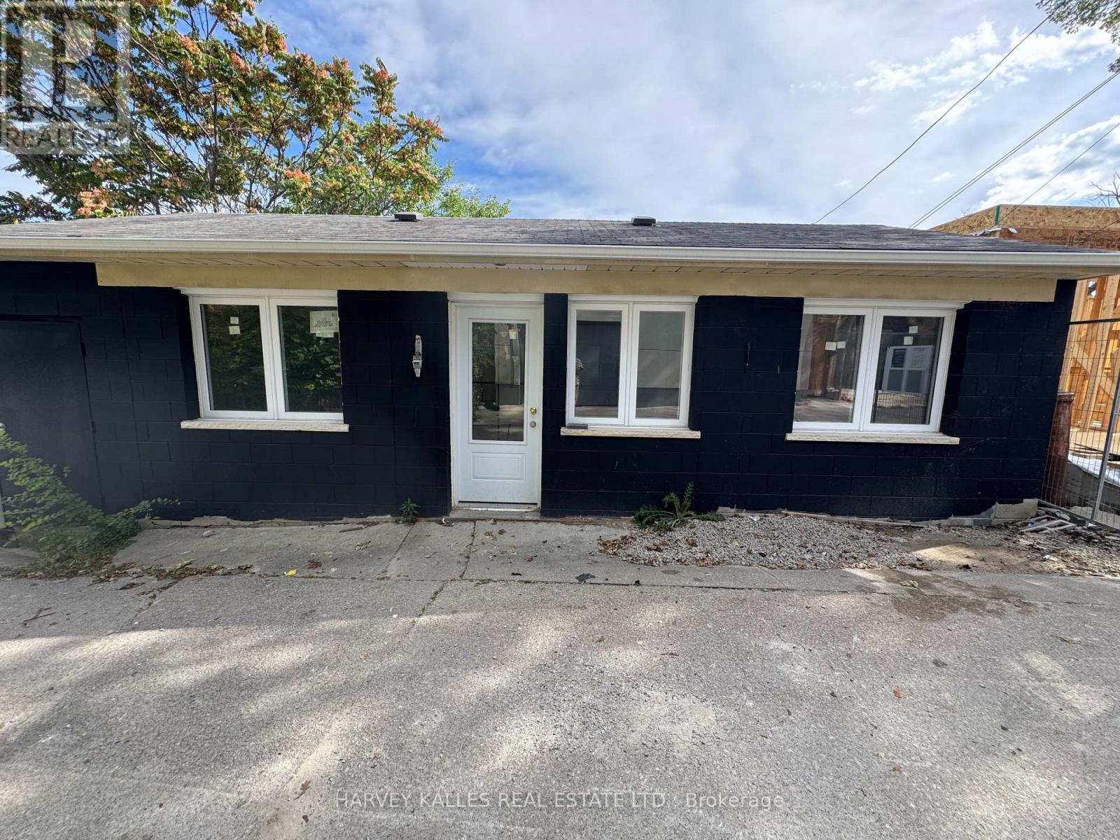 Single-story dark-sided house with white trim, a centered entrance door, and a paved driveway.