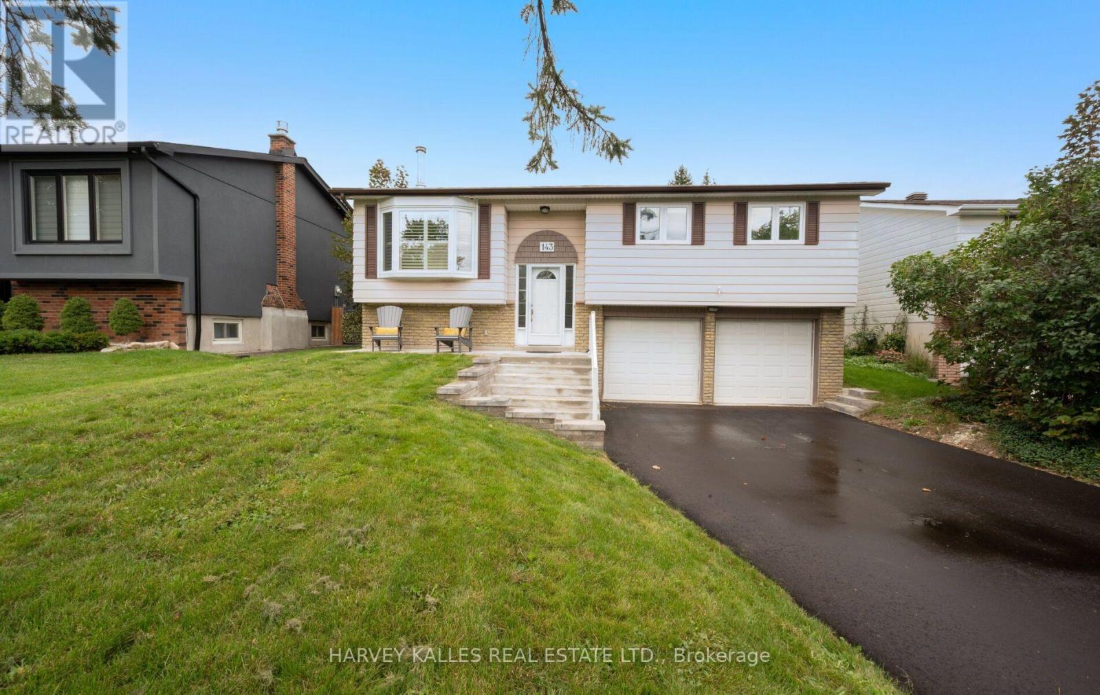 Raised bungalow with a brick lower level, two garage doors, front lawn, and paved driveway.