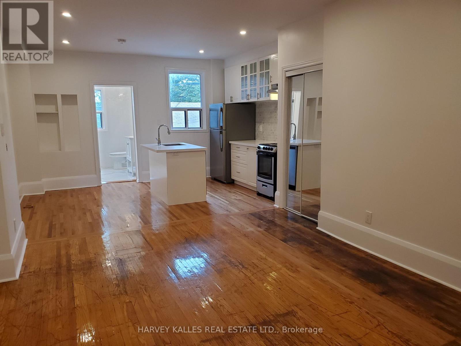 Open-plan kitchen with a central island, stainless steel appliances, and glossy hardwood floors.