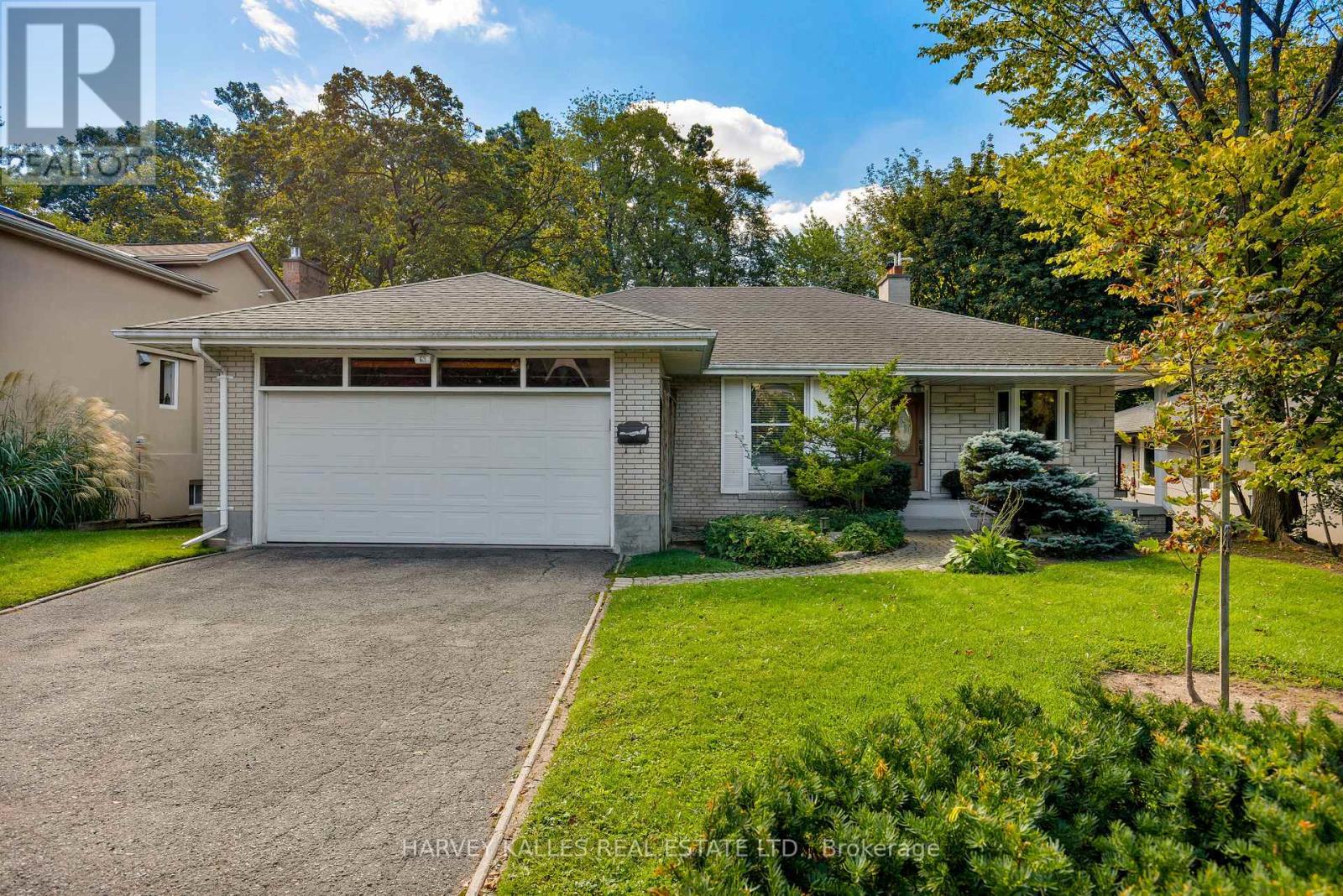 Single-story brick house with a double garage, paved driveway, landscaped lawn, and mature autumn trees.