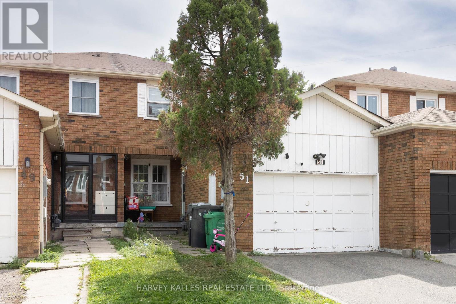 Brick townhouse with a white garage door and tall tree beside the front walkway.
