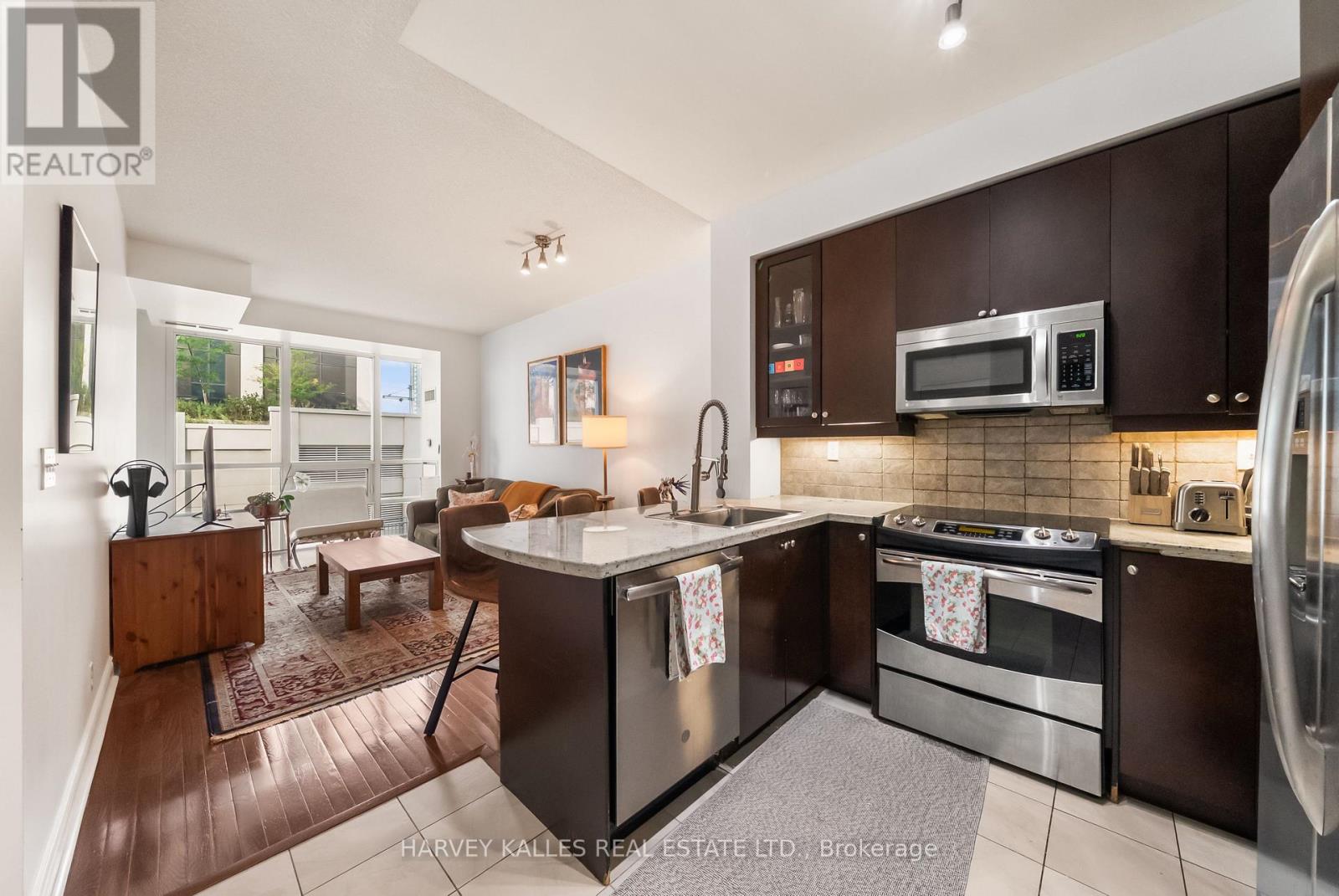 Open-plan condo kitchen with a stone island and stainless steel appliances beside the living area.