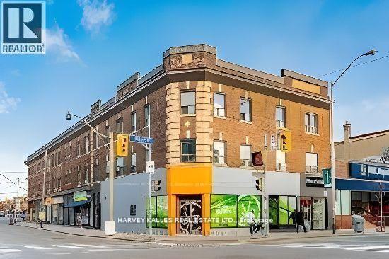 Two-story brick corner building with ground-floor storefronts, including a Harvey Kalles Real Estate office.